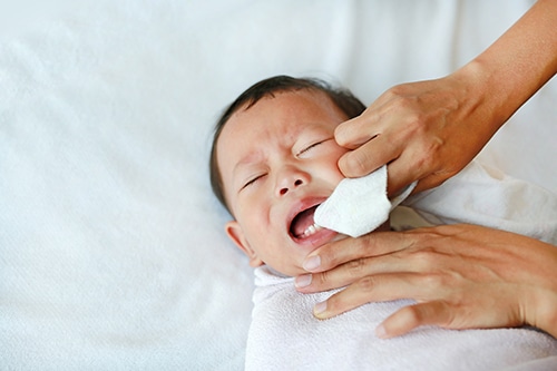 Tips for oral care for Babies. In this photo a parent wipes a baby's gums with a soft, clean cloth to wipe away bacteria and sugars that can cause cavities.