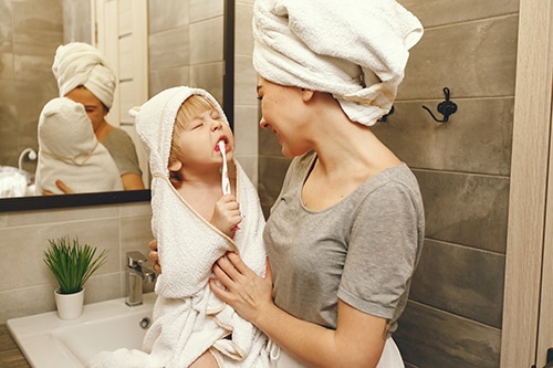 A mother teaches her young son to brush his teeth. It is teaching kids simple habits like this that have a huge life long effect. This is the gift that keeps on giving and your child will pass it on to their children, making good oral hygiene a family tradition.